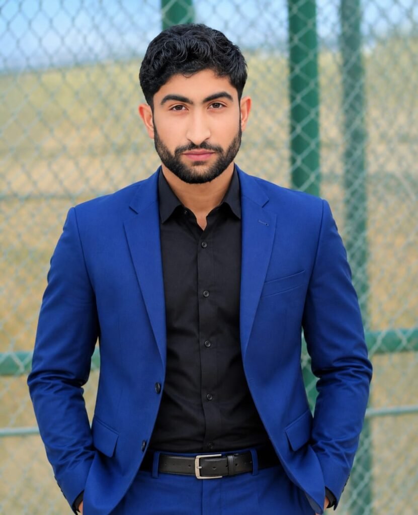 Young man wearing a blue suit and black shirt standing outdoors, looking at the camera with a professional appearance.